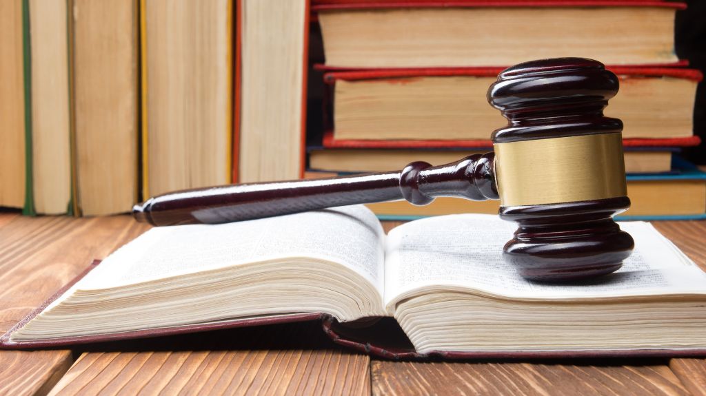 A gavel on top of an opened book with other books in the background