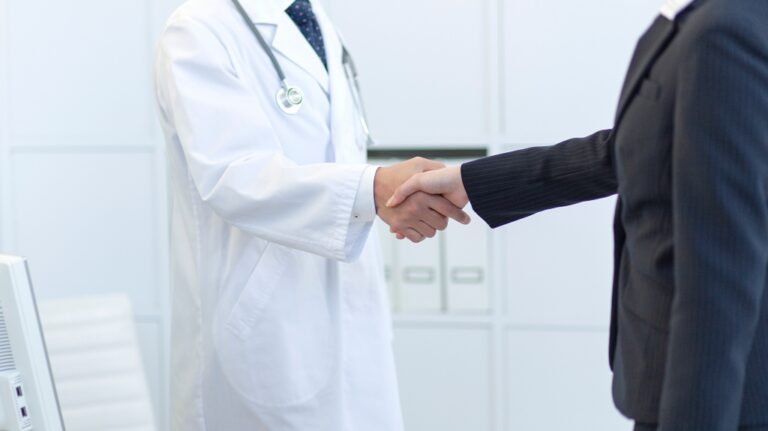 A businesswoman's hand shakes hands with a doctor in a white coat