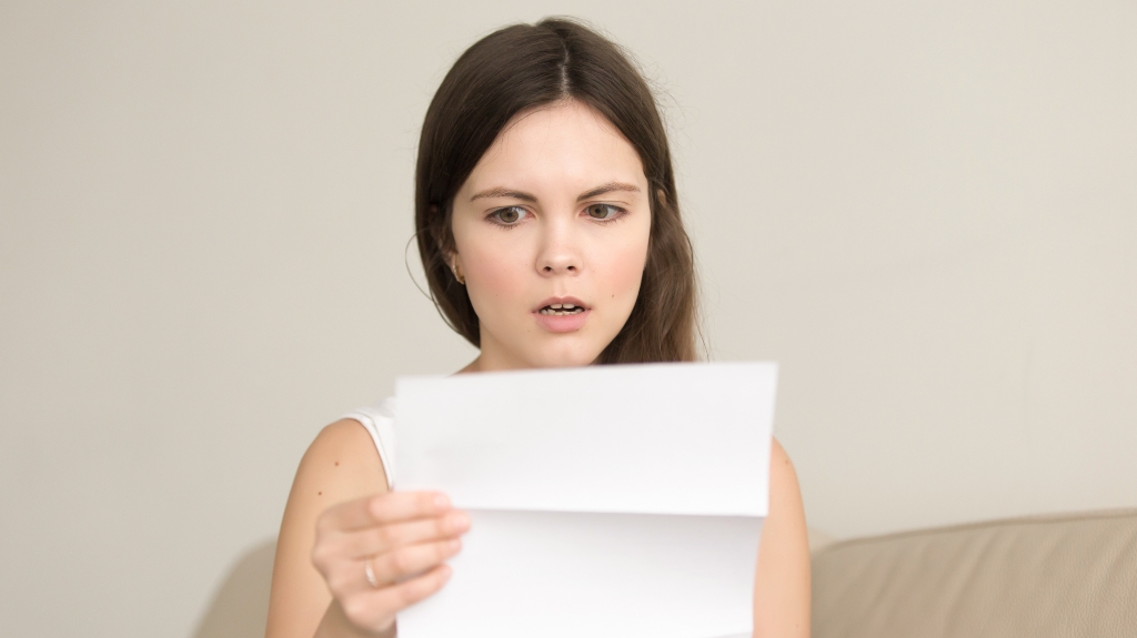 Surprised young woman reading letter with bad news